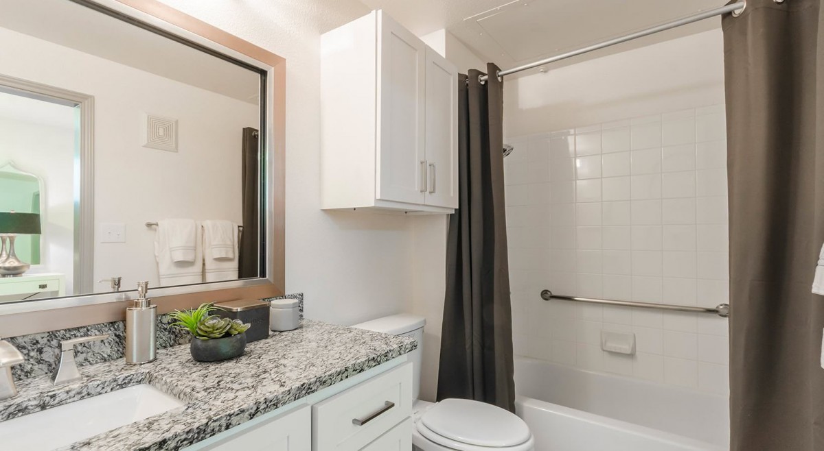 A modern bathroom featuring a granite countertop and white cabinetry, with a dark shower curtain complementing the clean design.