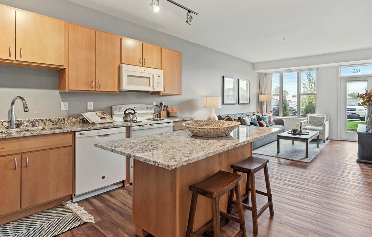 A contemporary open floor plan featuring a kitchen with a granite island and stools, flowing into a cozy living area.