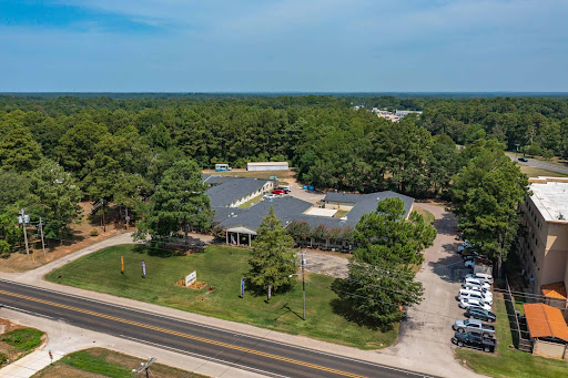 Aerial view of a commercial building surrounded by trees and a roadway.