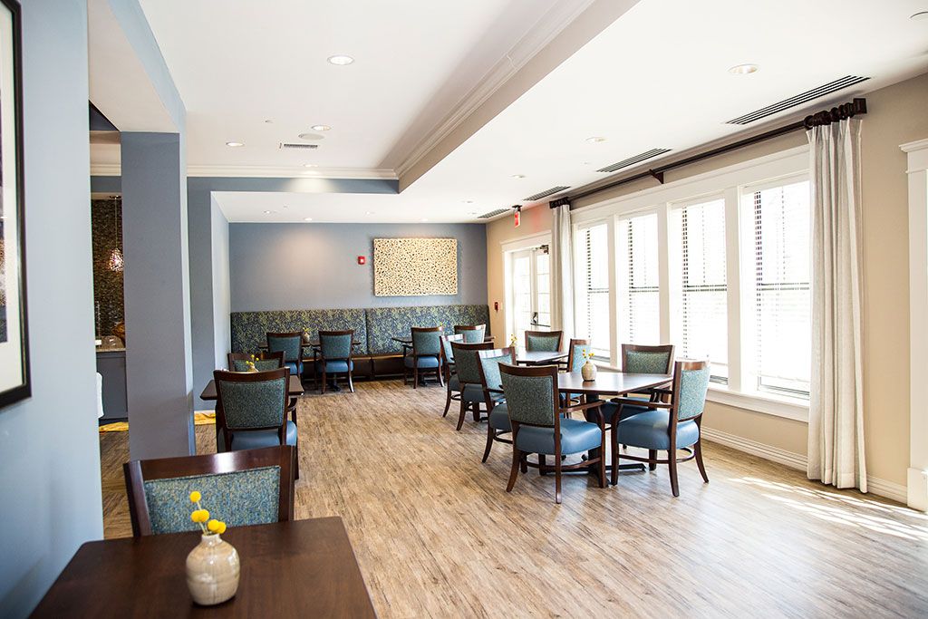 A well-lit dining room with modern decor, featuring tables and chairs near large windows.