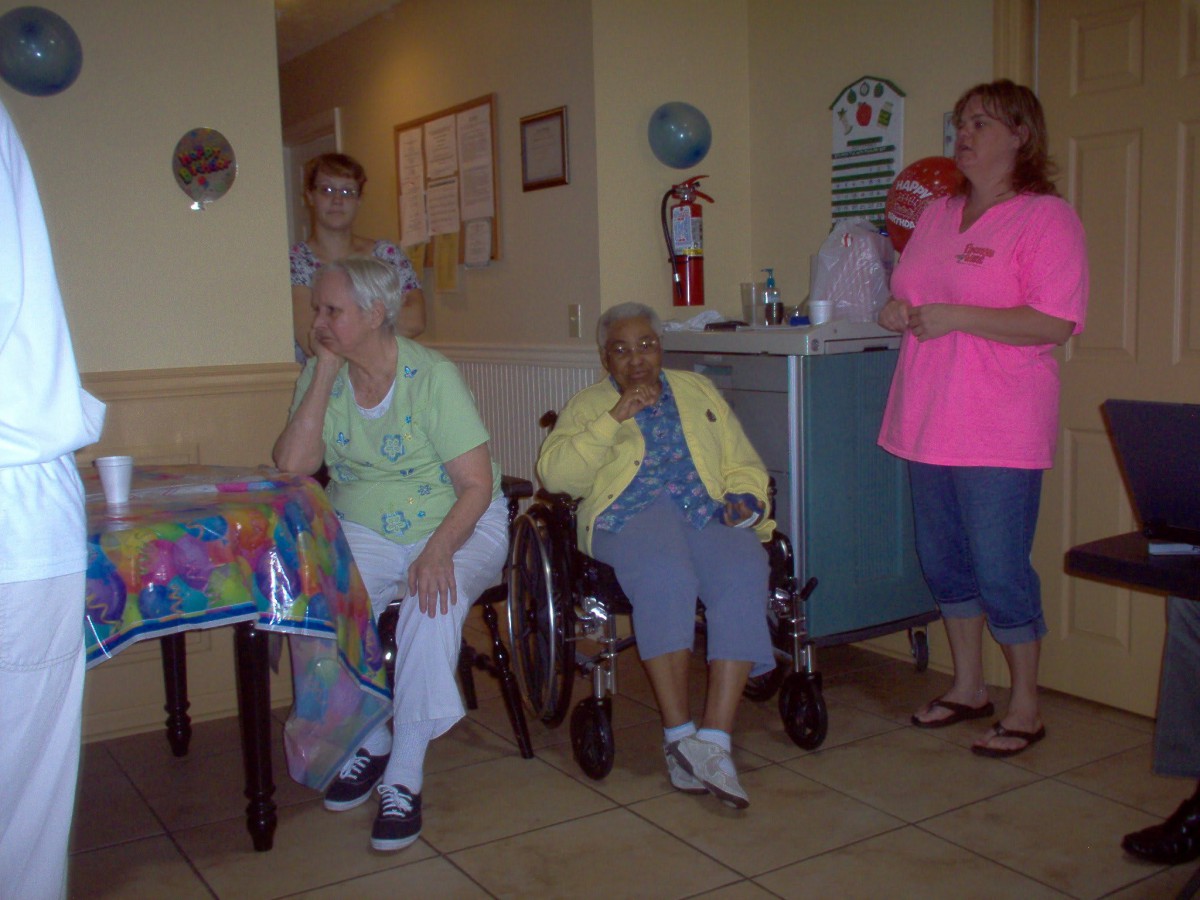 A group of elderly individuals celebrate a birthday indoors, with balloons and gifts.