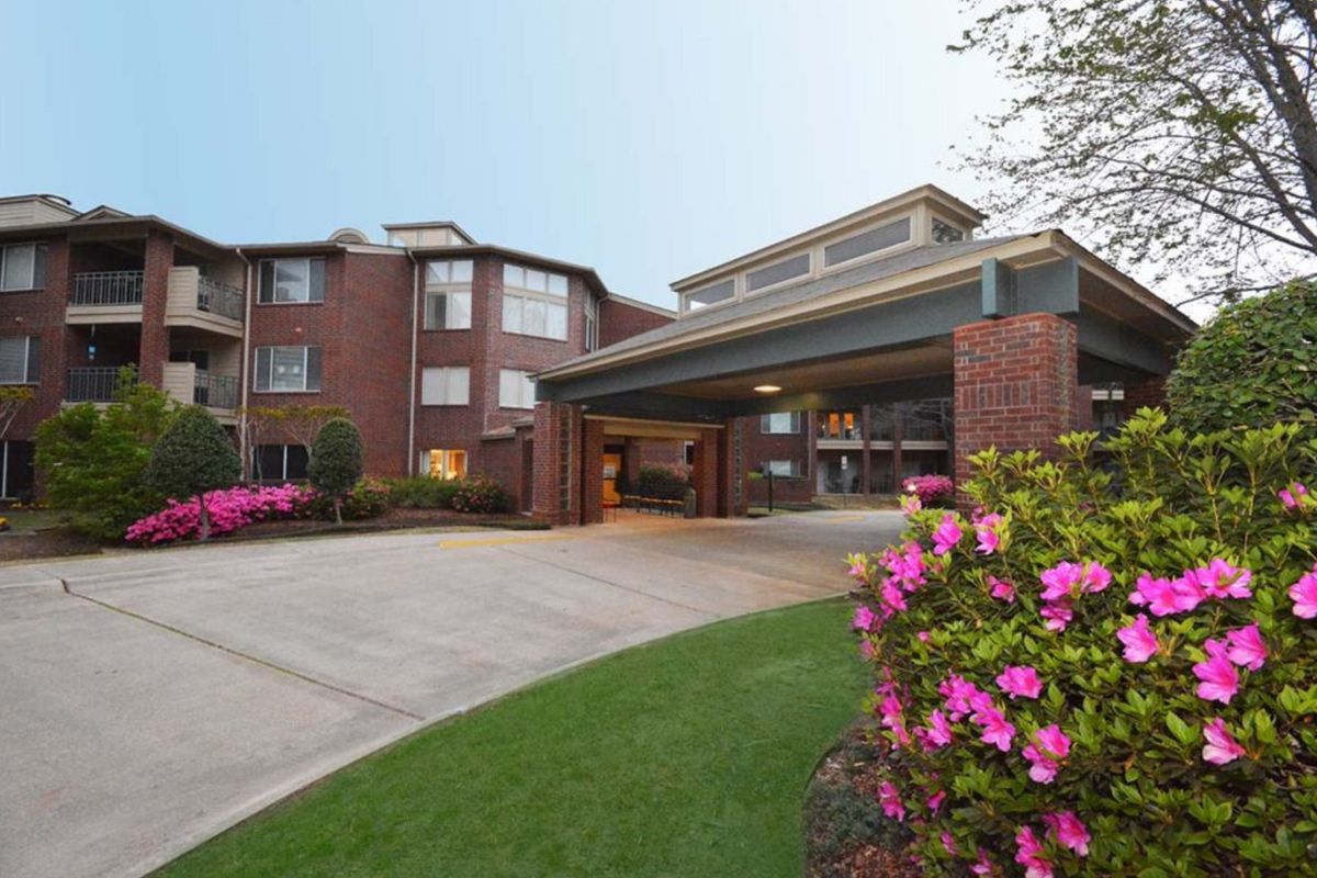A residential building with a landscaped entrance featuring blooming flowers and a driveway.