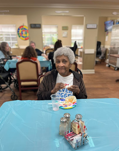 An elderly woman enjoying a meal in a communal dining setting, radiating joy and companionship.