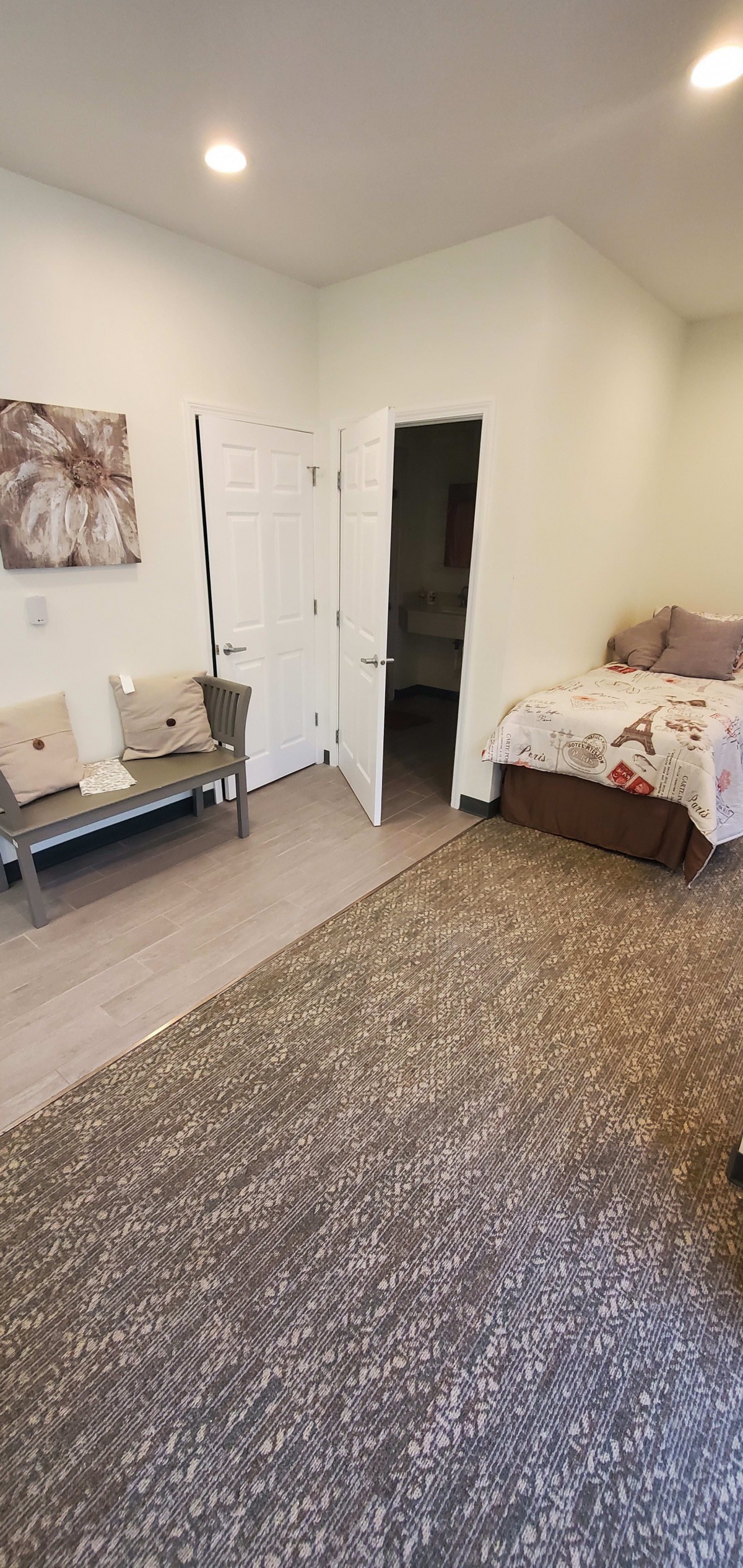 A minimalist bedroom with a single bed, chairs, a carpet, and wall art.