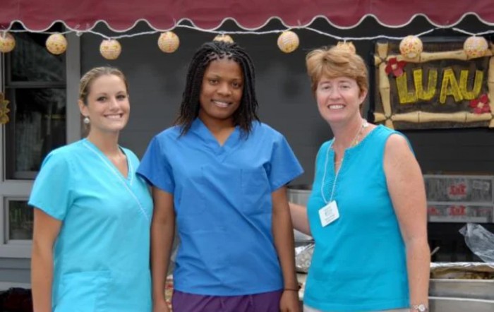 A group of three women smiling outdoors in casual attire.