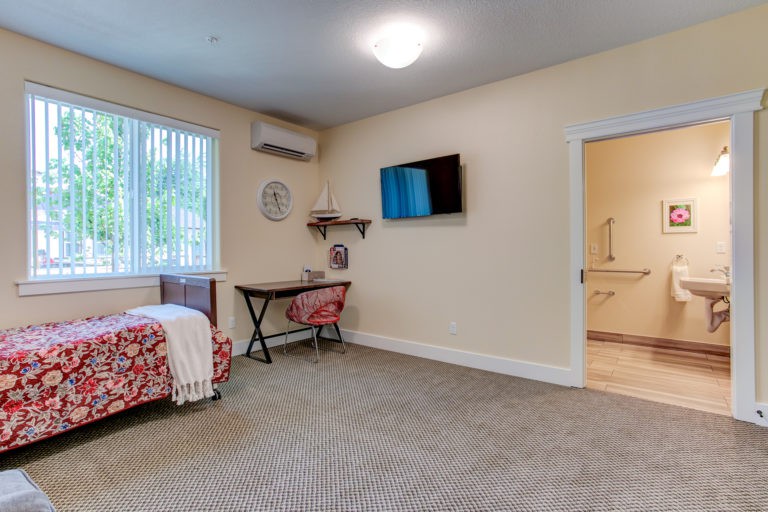 A cozy bedroom with a single bed, desk, and wall-mounted TV.