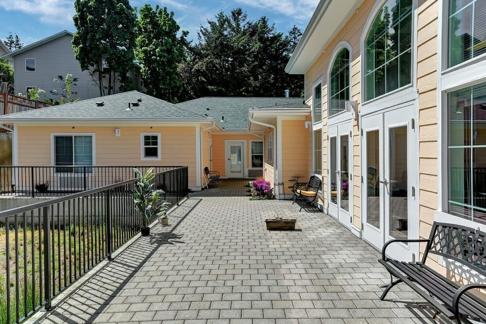 A spacious outdoor patio area next to a building, featuring potted plants and surrounded by tall trees.