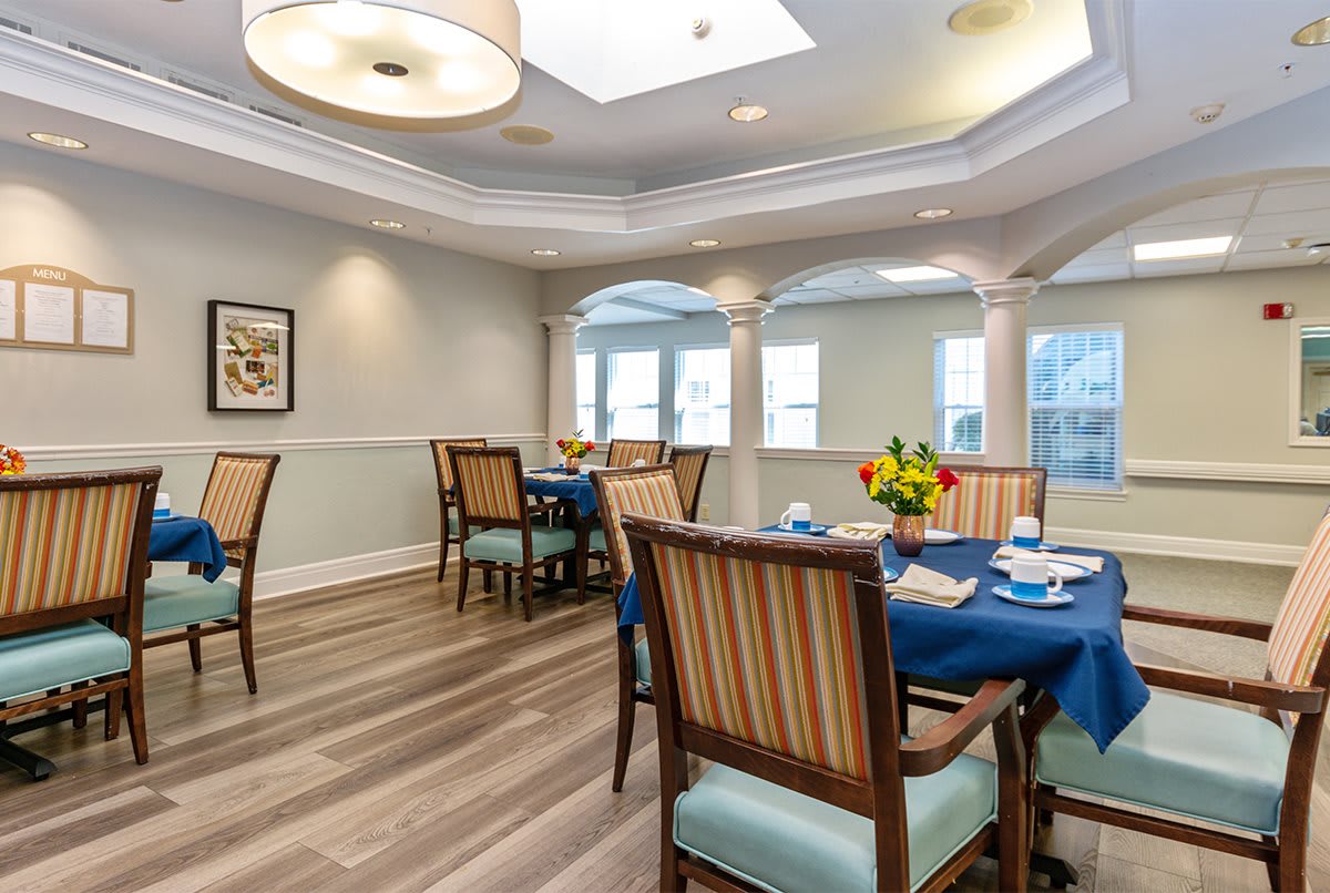 A well-lit dining area with several tables and chairs arranged, featuring elegant decor and large windows.