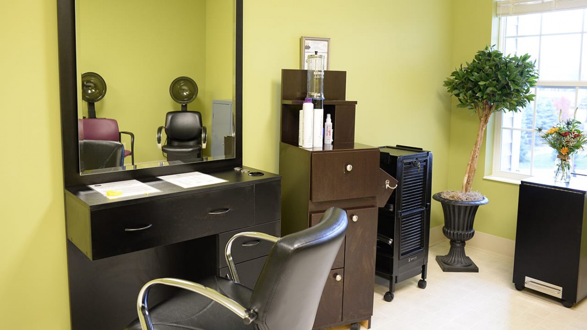 A neatly organized hair salon with a styling chair, mirror, and shelves for hair products.