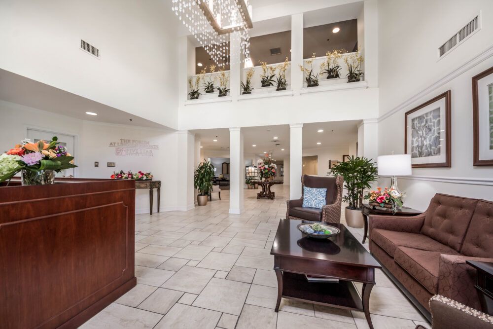 A spacious hotel lobby featuring a reception desk, elegant chandelier, and comfortable seating area with decorative plants.