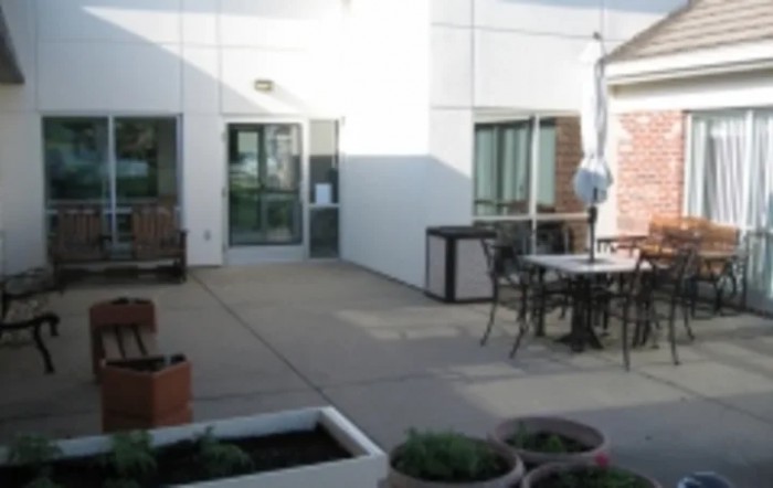 A patio area with tables, chairs, and planters outside a building.