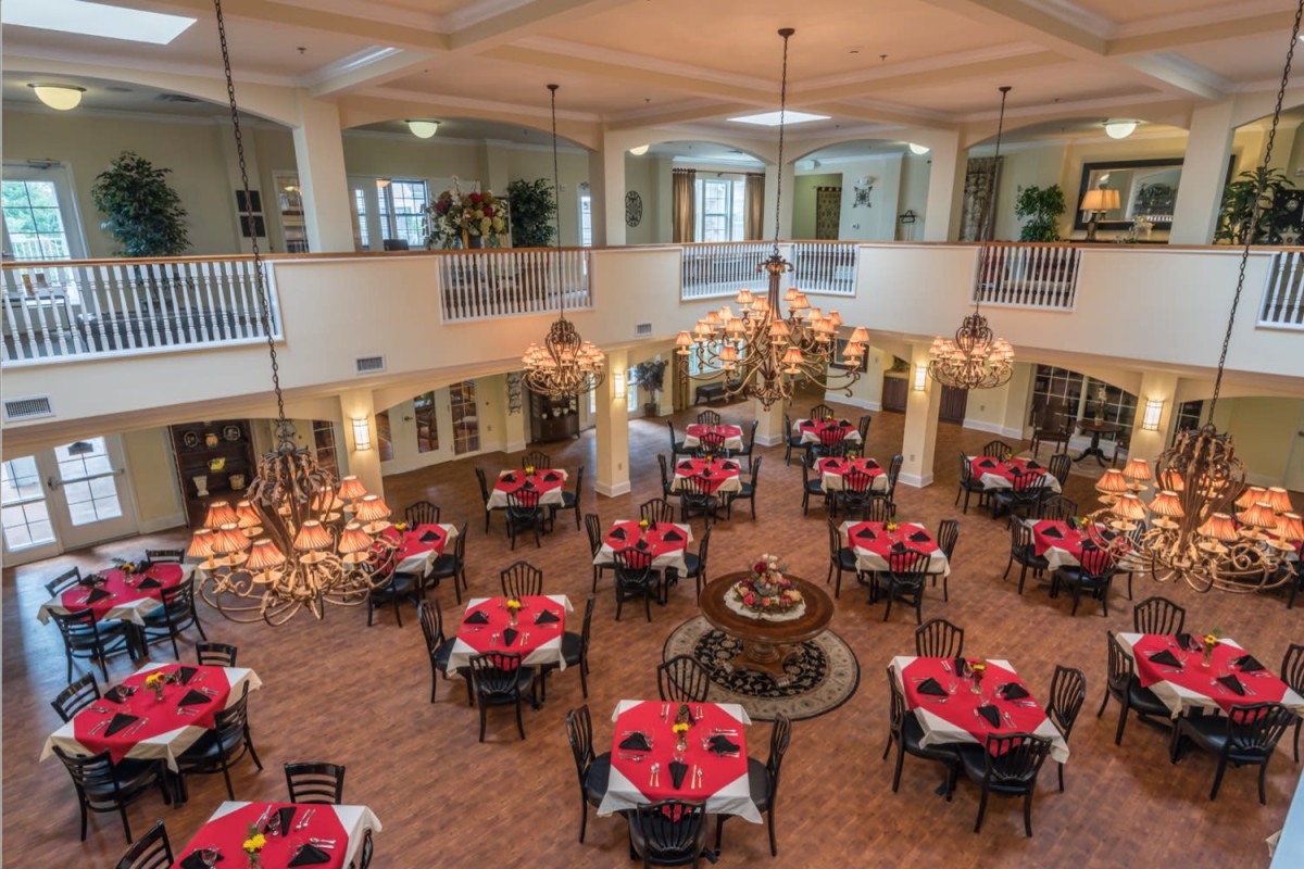 A spacious and elegant dining area featuring multiple tables with red tablecloths, ornate chandeliers, and a classic interior design.