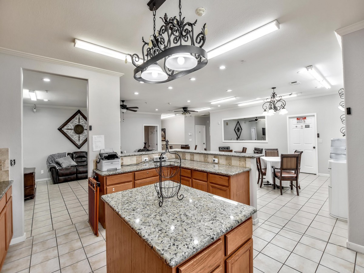 A spacious modern kitchen with granite countertops, a large island, wooden cabinets, and chandelier lighting.