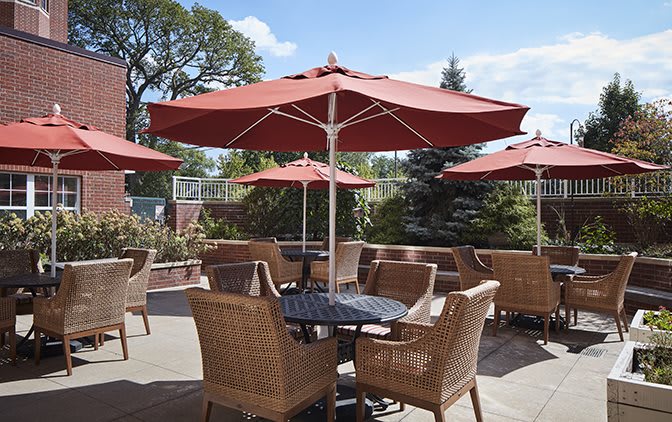 A cozy outdoor patio with wicker chairs and tables under large red umbrellas.