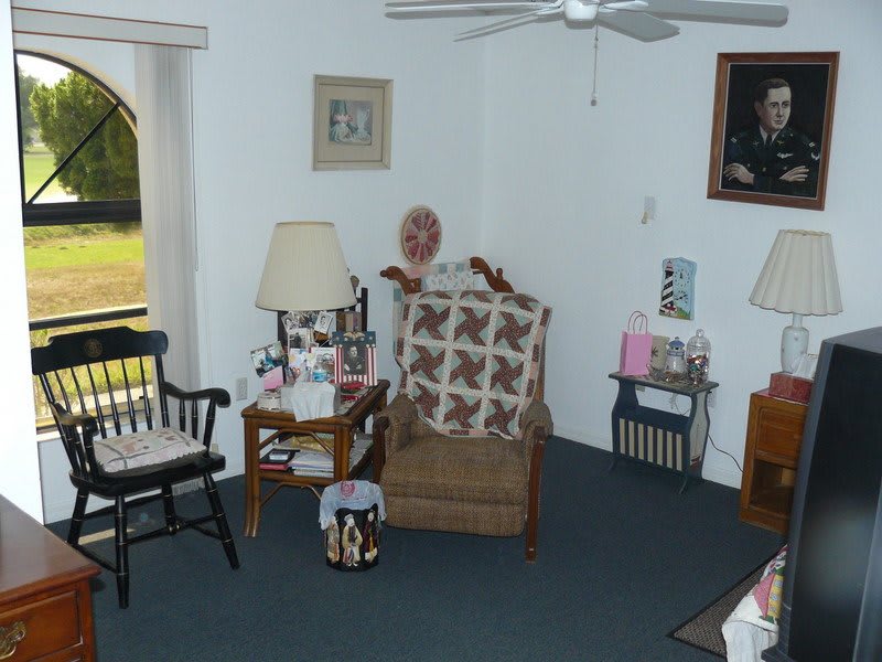 A cozy living room setting featuring a person sitting on a chair with a cushion, surrounded by various furniture and decor elements.