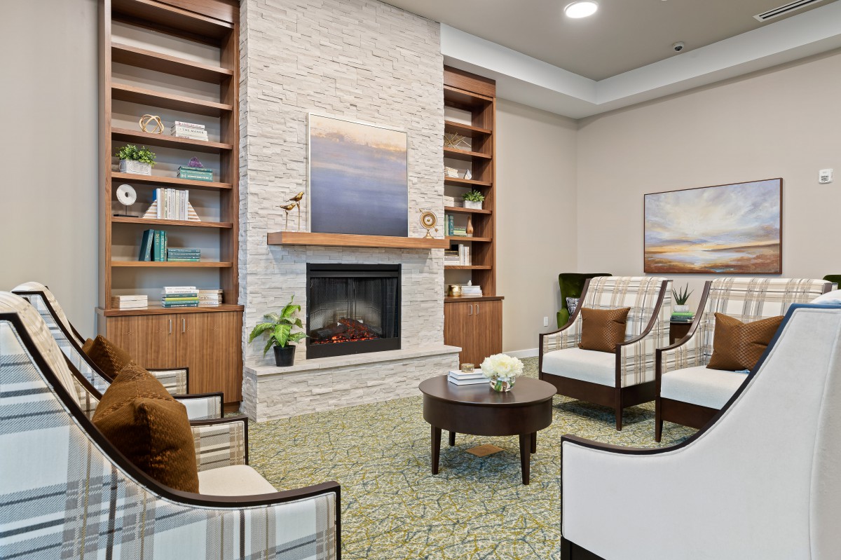 A modern and cozy living room with a fireplace, armchairs, and bookshelves.