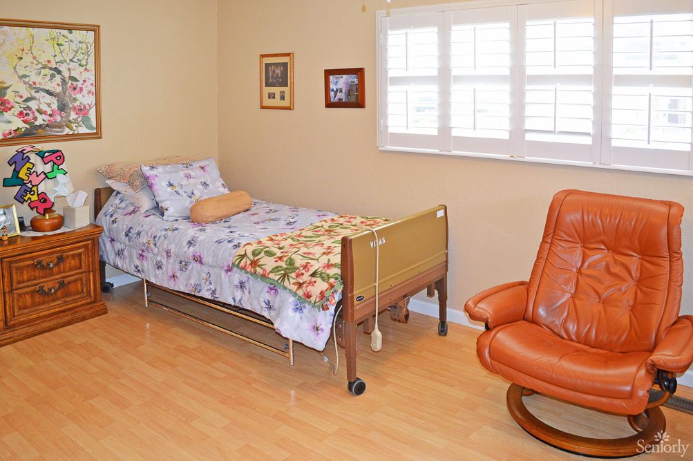 A cozy bedroom with a single bed, an orange armchair, and light wooden flooring.