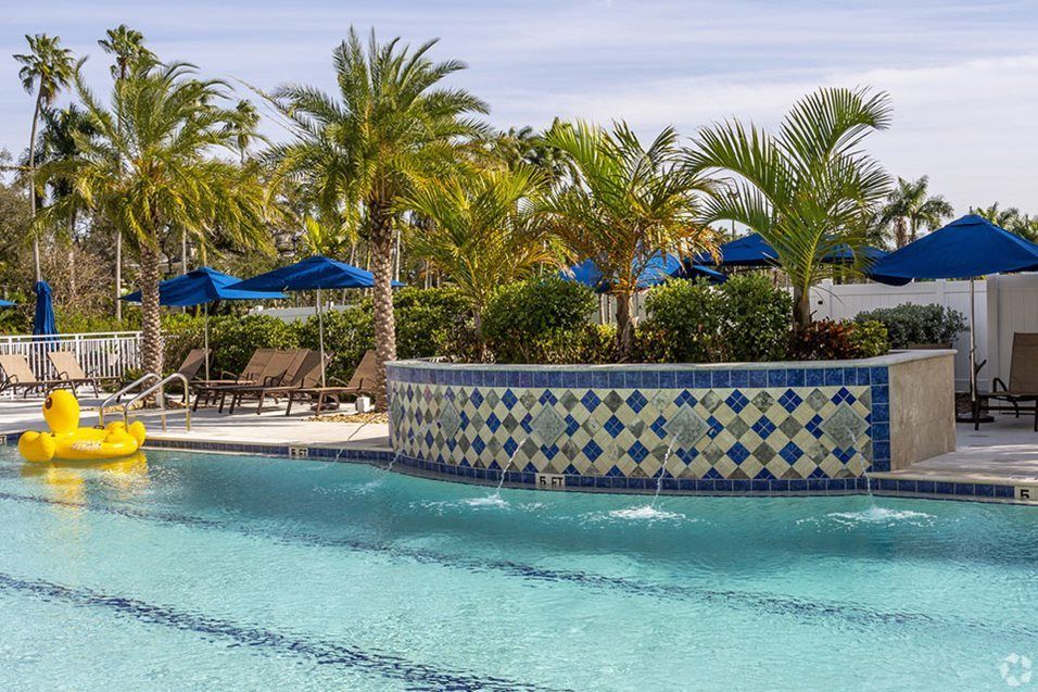 A tranquil view of a resort swimming pool surrounded by palm trees and blue umbrellas.