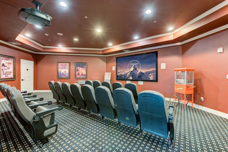 A home theater room with rows of comfortable seating facing a large screen, surrounded by movie posters and warm lighting.