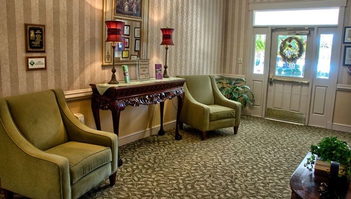 An elegant lobby area featuring two green chairs, a decorative wooden table with red lamps, and patterned carpet.