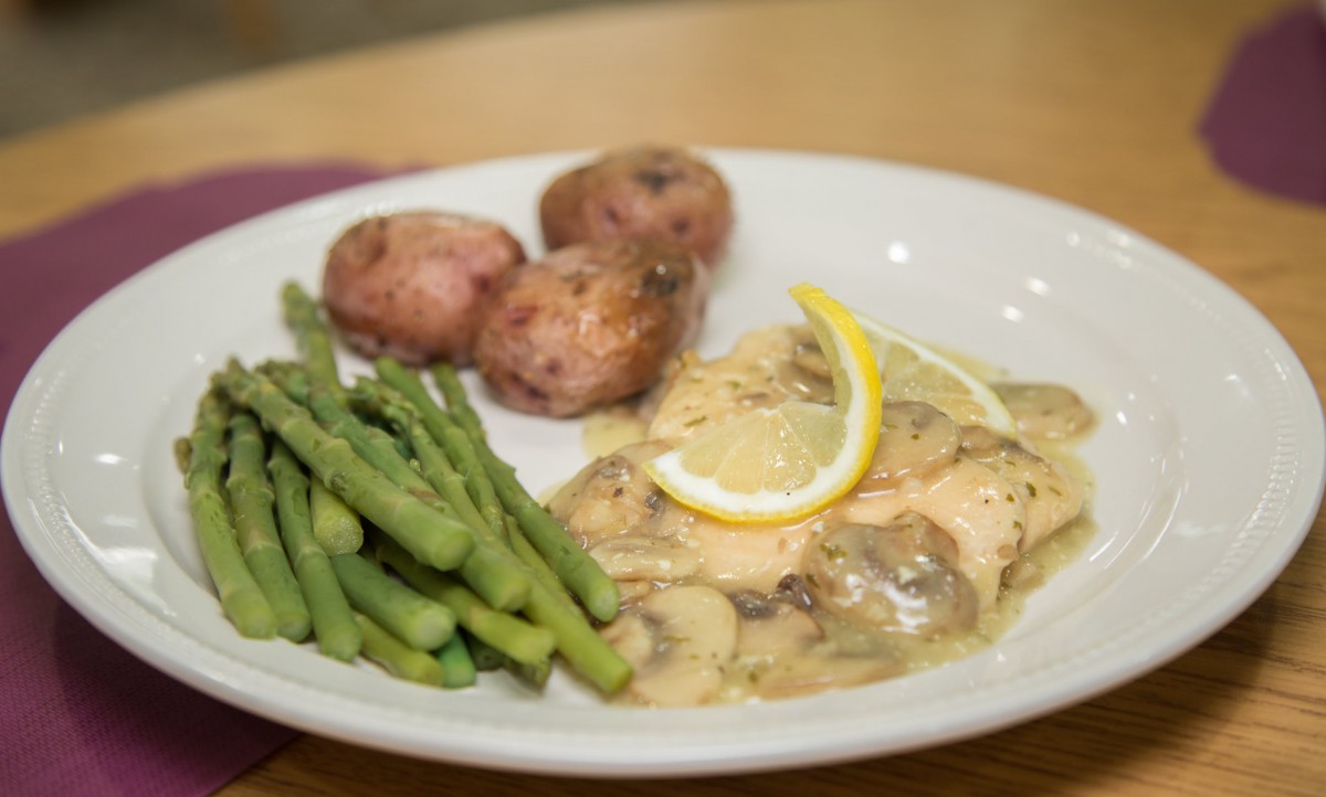 A plate of chicken with a creamy sauce, served with asparagus and red potatoes.