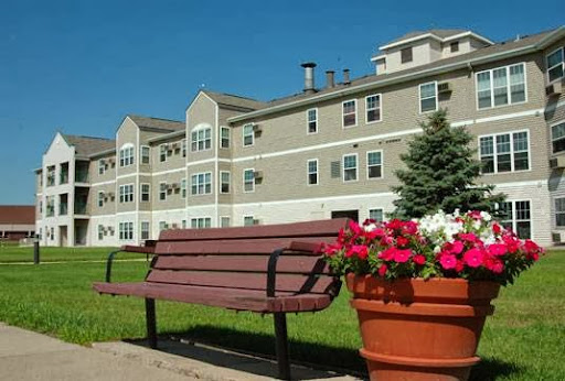 A serene view of an apartment building with a bench and colorful flowers in the foreground.