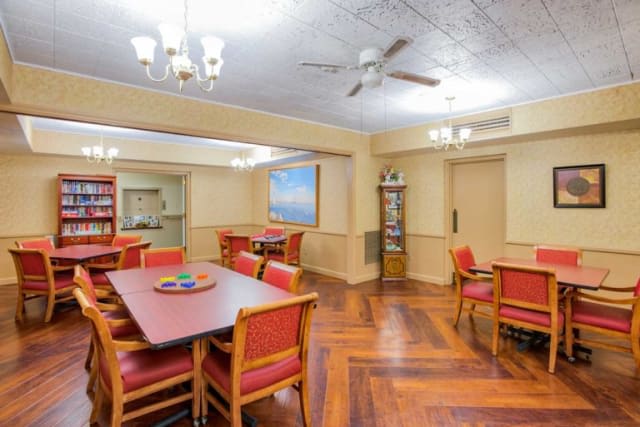 A cozy dining room with wooden floors, red cushioned chairs, and elegant lighting fixtures.