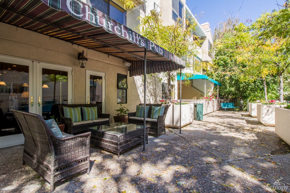 A cozy outdoor seating area at a cafe with wicker furniture and shade provided by awnings.
