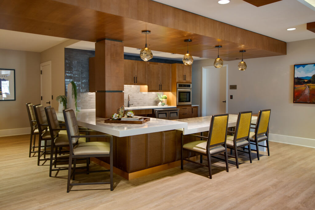 A modern kitchen with wooden cabinets and an island counter, featuring pendant lighting and a dining area.