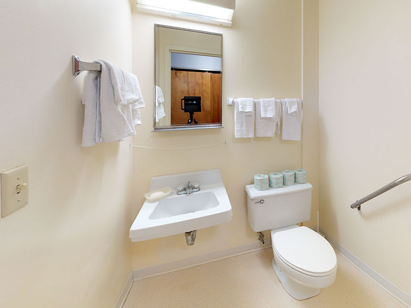 A minimalist bathroom with a sink, toilet, and neatly arranged towels.