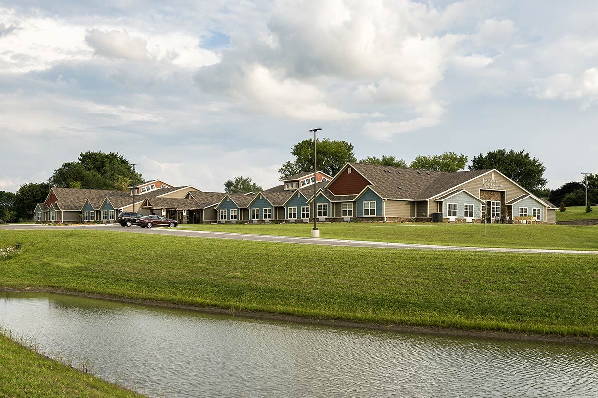 A picturesque residential area with houses and a pond under a partly cloudy sky.