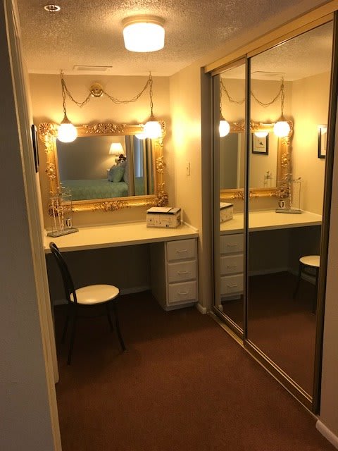 A well-lit vanity area with a mirror and desk, featuring elegant decor.
