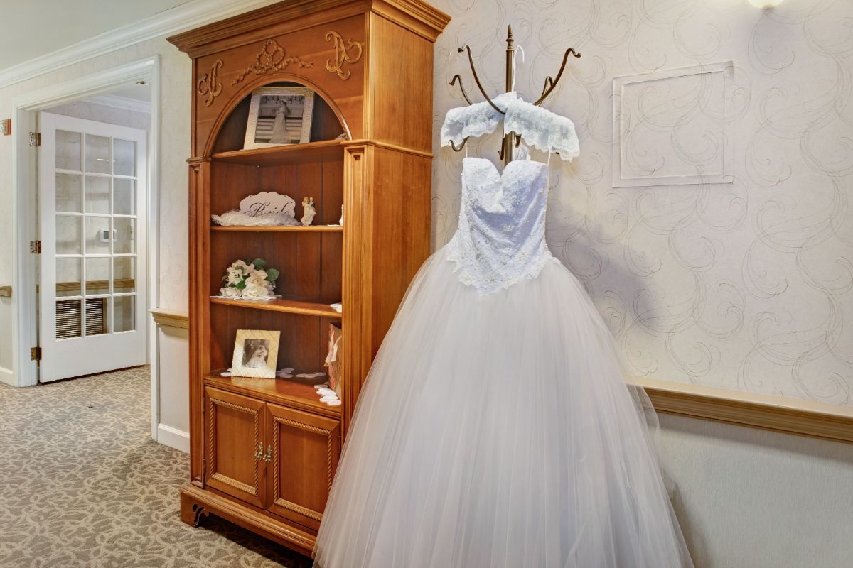 A beautiful white wedding dress displayed next to a wooden bookshelf.