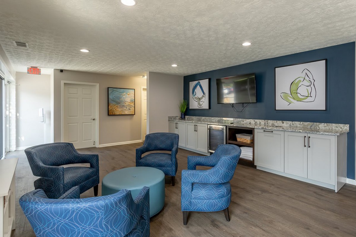 A modern living room with blue chairs and a coffee table, featuring contemporary artwork on the walls.