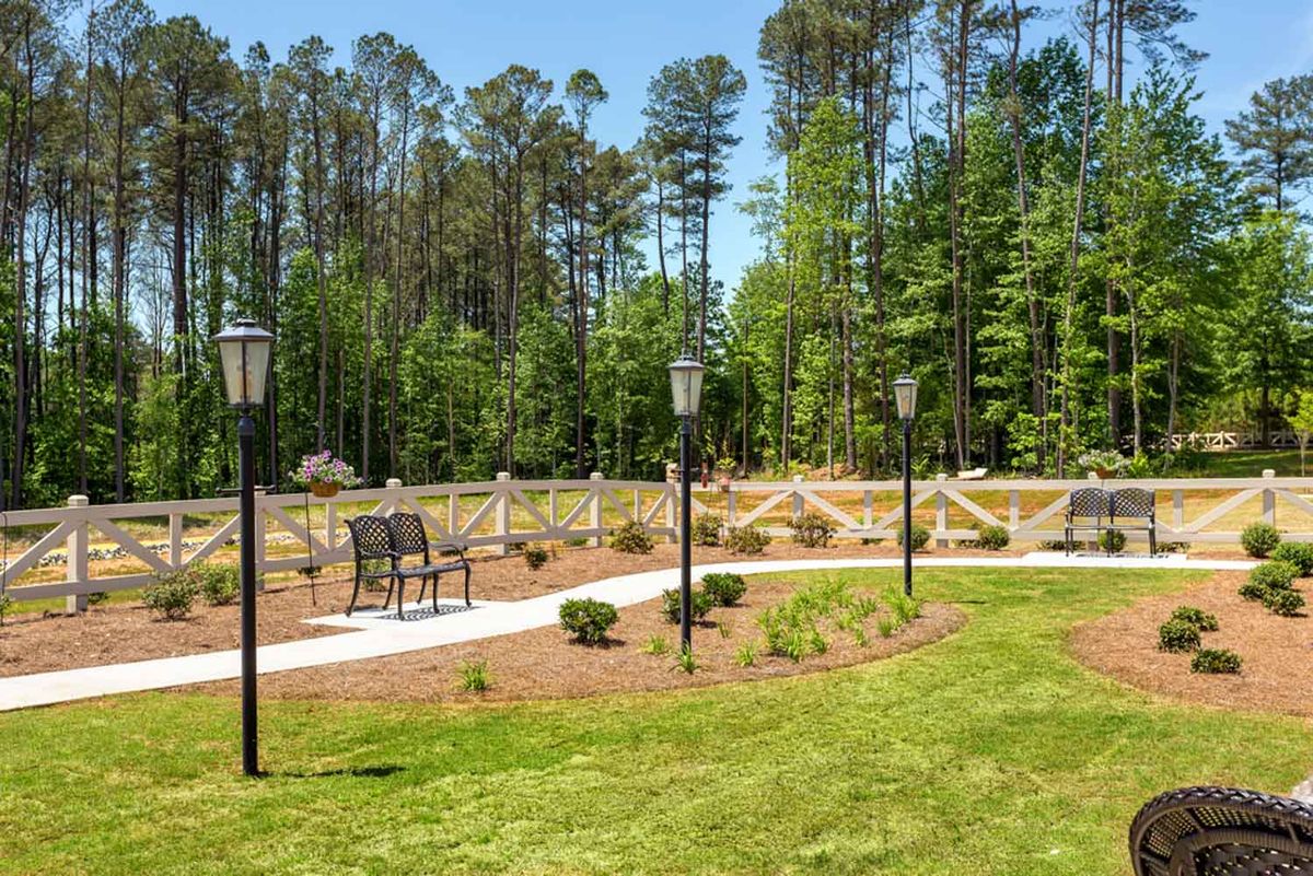 A scenic garden area with benches, lamp posts, and a winding pathway surrounded by trees.