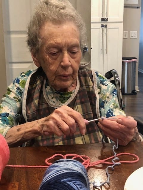 An elderly woman focused on knitting with colorful yarn.