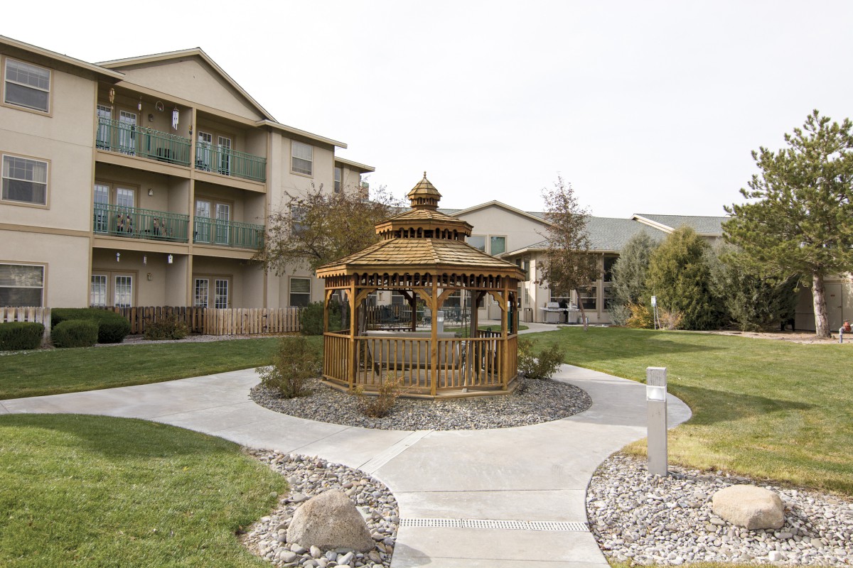 A wooden gazebo situated along a landscaped walkway in an apartment complex courtyard.