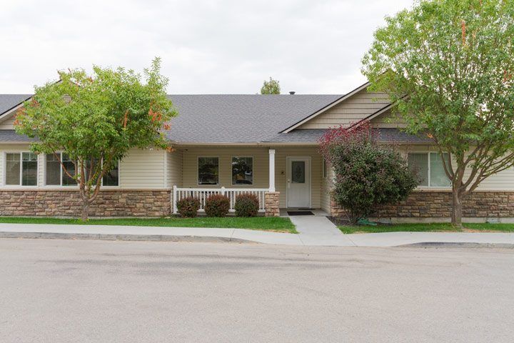 A suburban house with a porch and a small front yard surrounded by trees.