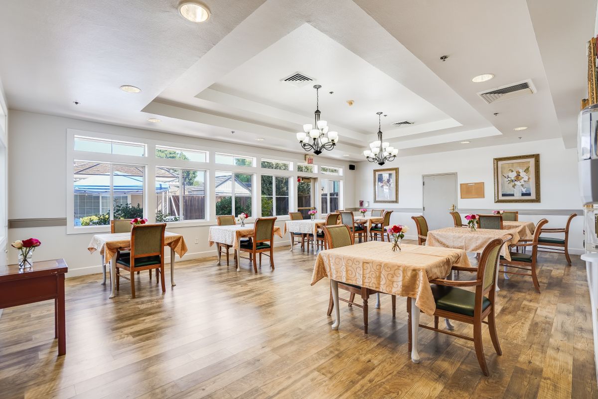 A bright and spacious dining room with multiple tables and chairs, adorned with chandeliers.