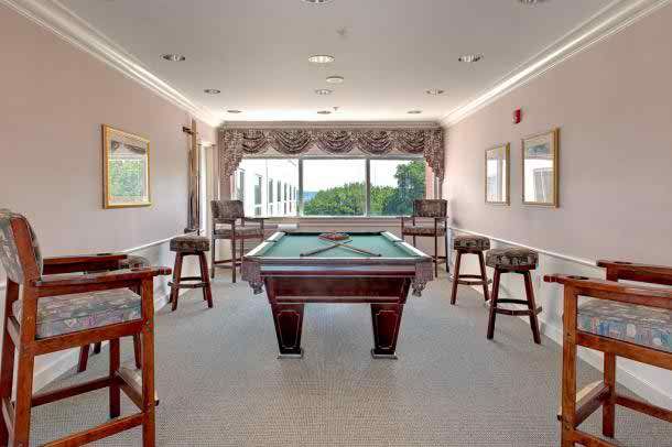 A well-lit game room featuring a pool table and bar stools, with large windows providing an outdoor view.