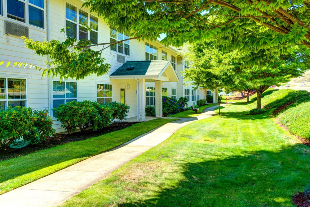 A sunny day in a residential area with an apartment building surrounded by lush green lawns and trees.