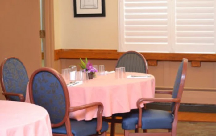 A cozy dining room with a round table covered in a pink tablecloth and surrounded by chairs.