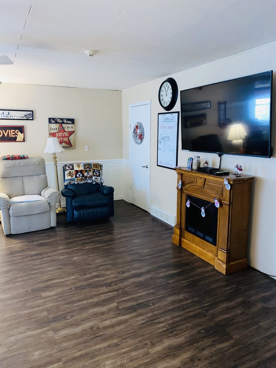 A cozy living room with seating, a large TV, and a decorative fireplace.