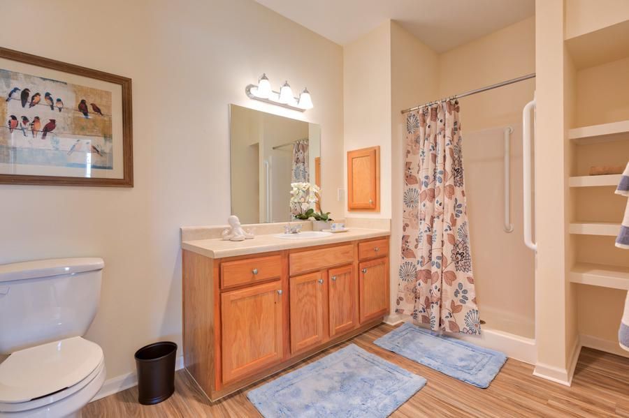 A tidy bathroom featuring a vanity with a mirror, wooden cabinets, and a shower.