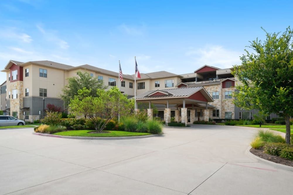 A view of a hotel building with a circular driveway and surrounding greenery.