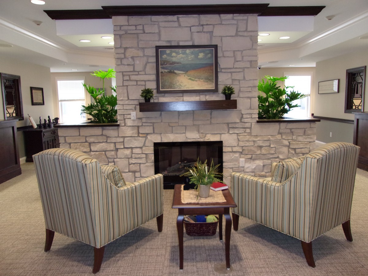A cozy living room setup featuring a stone fireplace flanked by two striped armchairs and decorated with lush green plants.