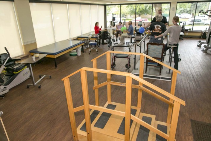 A rehabilitation center equipped with exercise equipment and therapy areas where people are engaged in physical therapy activities.