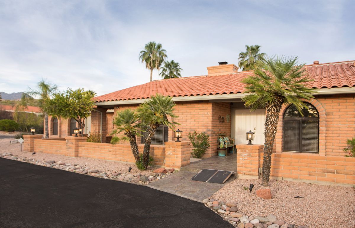 A single-story house with a brick exterior and palm trees in a desert landscape.
