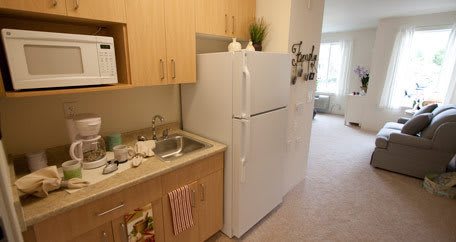A compact apartment kitchen with a refrigerator, sink, and wooden cabinets.