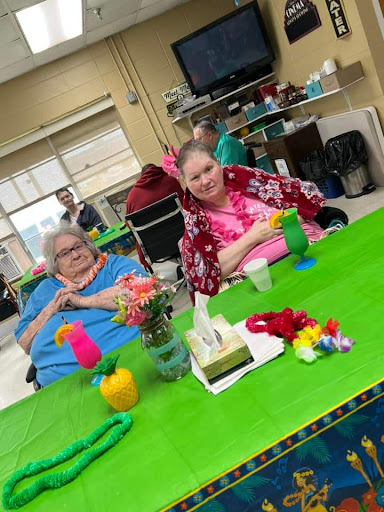 Two women enjoying a creative activity in a care facility, surrounded by colorful decorations and crafts.